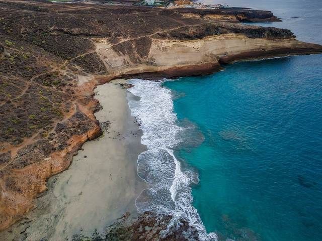 A secluded sandy cove between ochre cliffs on the Tenerife coast