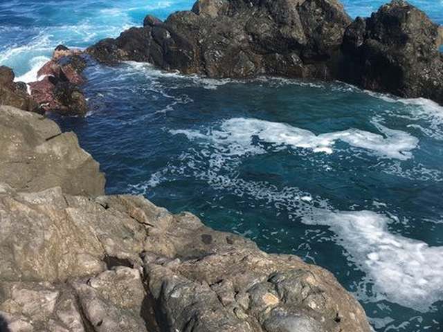 A turquoise natural volcanic pool in black lava rock by the ocean